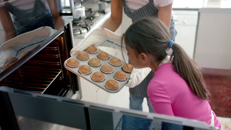 Happy-biracial-mother-and-daughter-baking-in-kitchen-taking-cakes-out-of-oven,-slow-motion