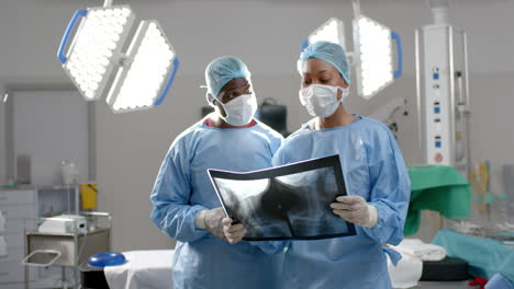 African-american-male-and-female-surgeons-looking-at-x-ray-scans-in-operating-theatre,-slow-motion