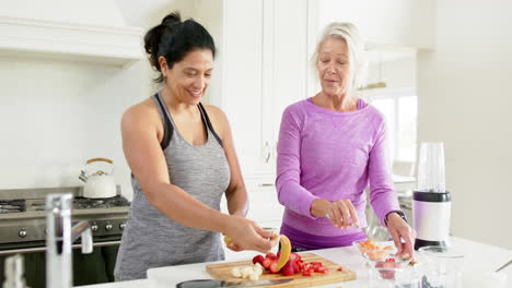 Zwei-Glückliche,-Vielfältige-Seniorinnen-Bereiten-Obst-Zu-Und-Lachen-In-Einer-Sonnigen-Küche,-Zeitlupe