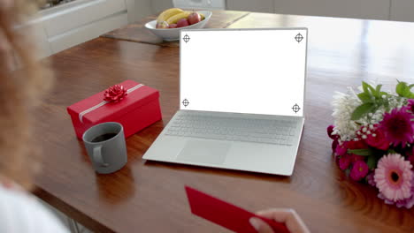 Caucasian-woman-holding-red-envelope-and-using-laptop-with-copy-space-on-blank-screen