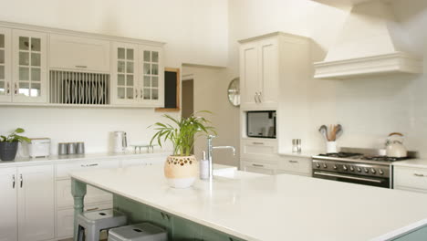 Kitchen-island,-sink,-oven,-gas-stove-and-white-furnitures-in-sunny-kitchen