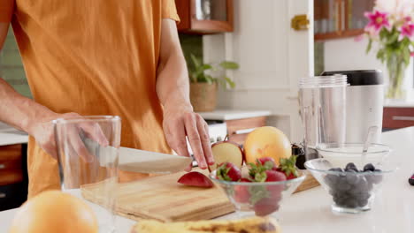 Midsection-of-biracial-man-chopping-fruit-for-healthy-smoothie-in-kitchen,-copy-space,-slow-motion