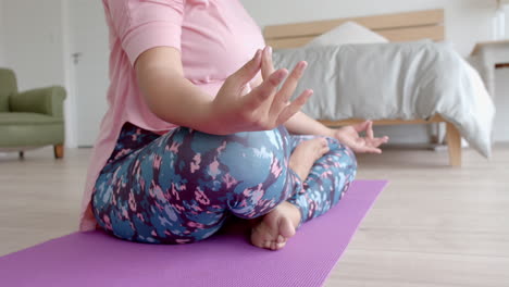 Midsection-of-plus-size-biracial-woman-sitting-on-floor-practicing-yoga-meditation,-slow-motion