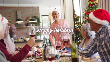 Animation-of-happy-holidays-text-over-diverse-senior-friends-sitting-at-table-at-christmas