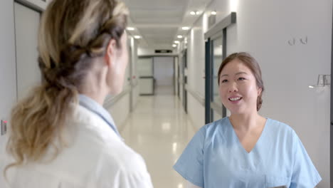 Happy-diverse-female-doctors-talking-in-hospital-corridor,-turning-and-smiling,-slow-motion
