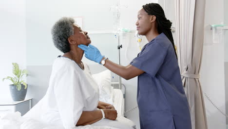 African-american-female-doctor-testing-neck-of-senior-female-patient-in-hospital-room,-slow-motion