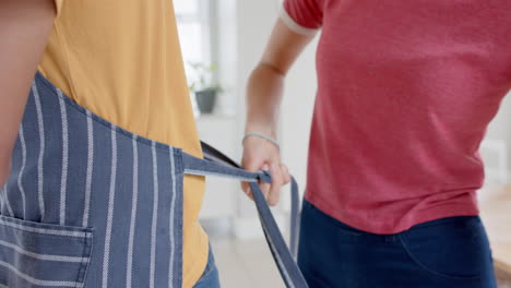 Diverse-couple-cooking-and-wearing-aprons-in-kitchen,-slow-motion