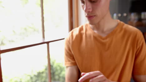 Thoughtful-biracial-man-using-tablet-by-window-in-living-room,-copy-space,-slow-motion