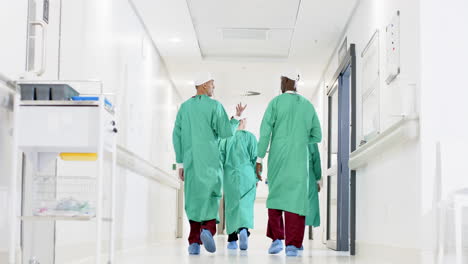 Diverse-male-and-female-surgeons-wearing-surgical-gowns-walking-in-corridor-at-hospital,-slow-motion