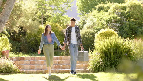 Happy-diverse-couple-holding-hands-and-walking-in-sunny-garden,-in-slow-motion