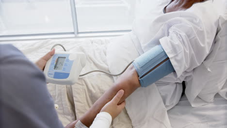Diverse-female-doctor-testing-blood-pressure-of-senior-female-patient-in-hospital-room,-slow-motion