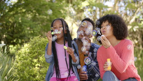 Happy-african-american-parents-with-daughter-blowing-bubbles-in-garden-at-home,-slow-motion