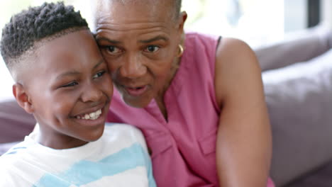 Glücklicher-Afroamerikanischer-Enkel-Und-Großmutter-Reden-Und-Umarmen-Sich-Auf-Dem-Sofa,-Zeitlupe