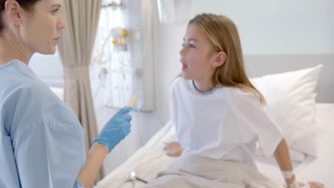 Caucasian-female-doctor-in-gloves-with-spatula-checking-throat-of-girl-hospital-patient,-slow-motion
