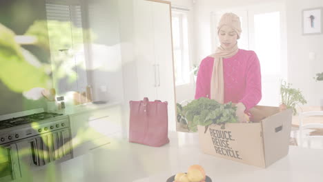 Biracial-woman-in-hijab-with-box-with-vegetables-in-kitchen,-over-leaves
