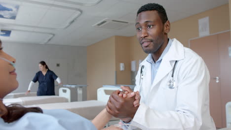 Diverse-male-doctor-holding-hand-of-female-patient-with-oximeter-in-hospital-bed,-slow-motion