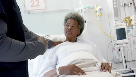 African-american-male-doctor-talking-with-female-senior-patient-in-hospital-room,-slow-motion
