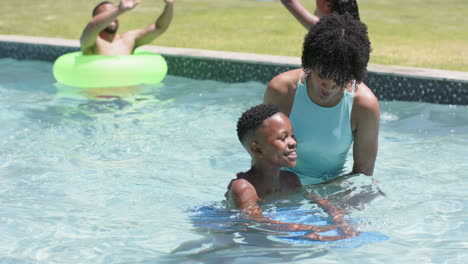 Afroamerikanische-Mutter-Bringt-Sohn-Das-Schwimmen-Mit-Schwimmkörper-Im-Sonnigen-Pool-Bei,-Zeitlupe