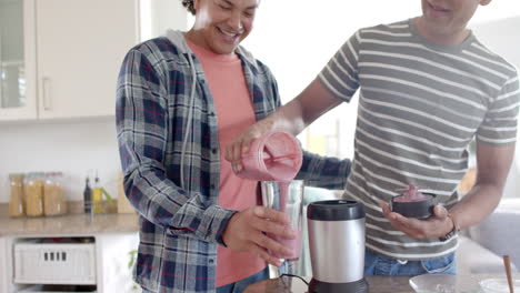 Happy-diverse-gay-male-couple-pouring-healthy-fruit-smoothie-in-kitchen,-slow-motion