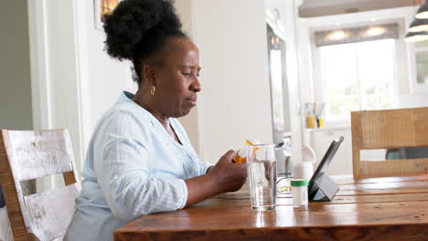 Mujer-Mayor-Afroamericana-Teniendo-Videollamadas-Y-Sosteniendo-Medicamentos-En-Una-Habitación-Soleada,-Cámara-Lenta