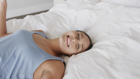 Portrait-of-happy-biracial-woman-lying-on-bed-at-home,-slow-motion