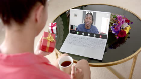 Biracial-woman-holding-gift-and-talking-with-biracial-man-talking-on-laptop-screen