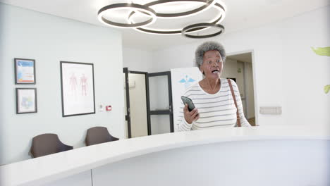African-american-senior-woman-with-smartphone-talking-in-hospital-reception,-slow-motion