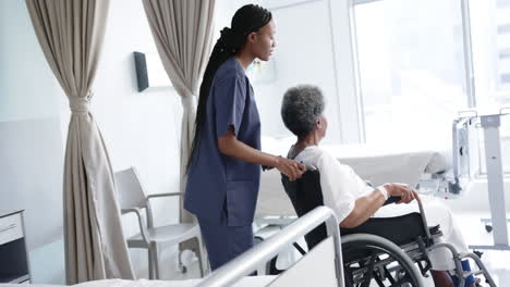 African-american-female-doctor-talking-with-senior-woman-in-wheelchair-in-hospital-room,-slow-motion