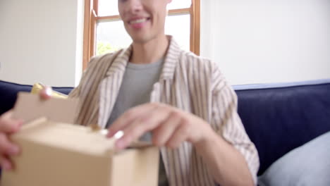 Excited-biracial-man-opening-delivery-in-cardboard-box,-slow-motion