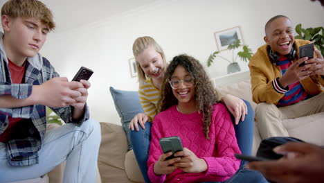 Happy-diverse-group-of-teenage-friends-using-smartphones-and-laughing-at-home,-slow-motion