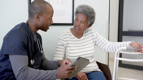 African-american-male-doctor-using-tablet-and-talking-with-senior-woman-in-hospital,-slow-motion