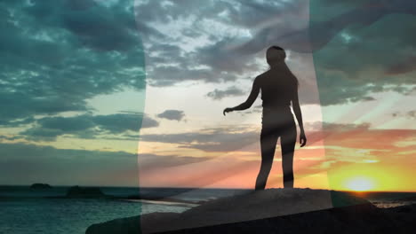 Animation-of-flag-of-nigeria-over-happy-caucasian-woman-climbing-on-rocks-and-viewing-sunset-beach