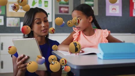 Animation-of-emoji-icons-over-biracial-schoolgirl-and-teacher-using-tablet