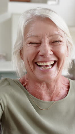 Happy-caucasian-senior-woman-having-video-call-and-blowing-kiss-in-sunny-room,-slow-motion