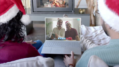 Happy-diverse-couple-and-male-relatives-having-christmas-laptop-video-call,-slow-motion