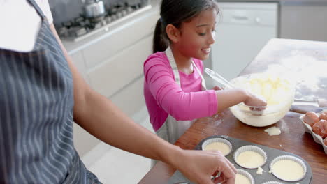 Happy-biracial-daughter-tasting-cake-mix,-baking-with-mother-in-kitchen,-slow-motion