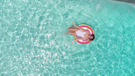 Aerial-of-happy-african-american-teenage-girl-playing-on-inflatable-in-sunny-pool,-copy-space