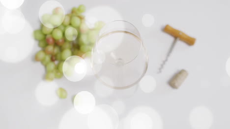 Composite-of-glass-of-white-wine,-corkscrew-and-white-grapes-over-spots-of-light-on-white-background