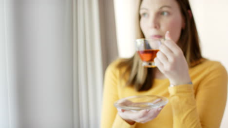 Thoughtful-caucasian-woman-drinking-tea-and-looking-through-window-at-home,-in-slow-motion