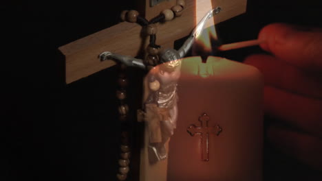 Animation-of-cross-with-rosary-over-hand-lighting-candle-on-black-background