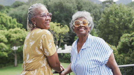 Portrait-of-senior-african-american-female-friends-in-sunglasses-laughing-on-balcony,-slow-motion