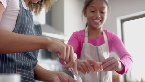 Happy-biracial-mother-and-daughter-making-cake-mix,-baking-in-kitchen,-slow-motion