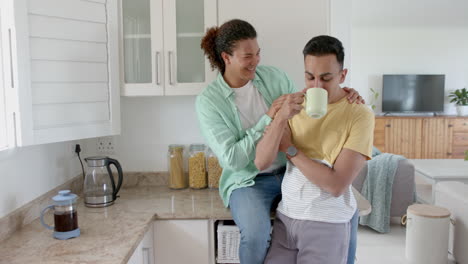 Happy-diverse-gay-male-couple-having-coffee-and-embracing-in-kitchen,-copy-space,-slow-motion