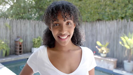 Happy-biracial-woman-with-long-curly-hair-in-white-t-shirt,-smiling-in-sunny-garden,-slow-motion