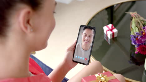 Caucasian-woman-holding-gift-and-smartphone-with-caucasian-man-on-screen