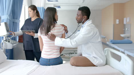 Diverse-male-doctor-using-stethoscope-on-back-of-female-patient-in-hospital,-copy-space,-slow-motion