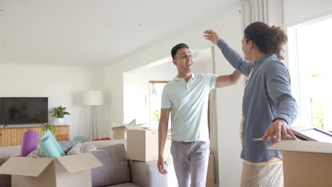 Happy-diverse-gay-male-couple-embracing-in-new-home-with-packing-boxes,-copy-space,-slow-motion