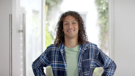 Portrait-of-happy-biracial-man-with-long-curly-dark-hair-in-doorway-at-home,-slow-motion