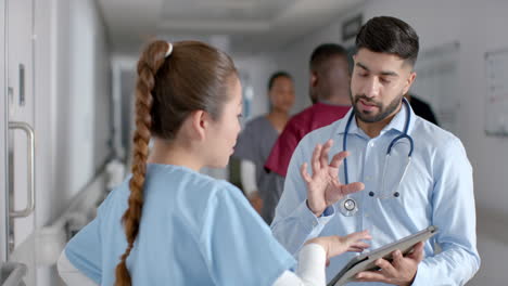Diverse-male-and-female-doctors-discussing-work-using-tablet-in-hospital-corridor,-slow-motion