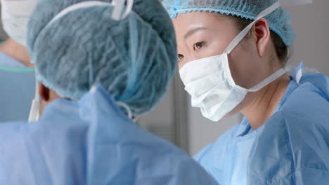 Diverse-female-surgeons-wearing-surgical-gowns-discussing-work-in-operating-theatre,-slow-motion